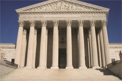 [ai] The front view of a large neoclassical building with six prominent columns and a triangular pediment, leading up to a set of steps under a clear blue sky.